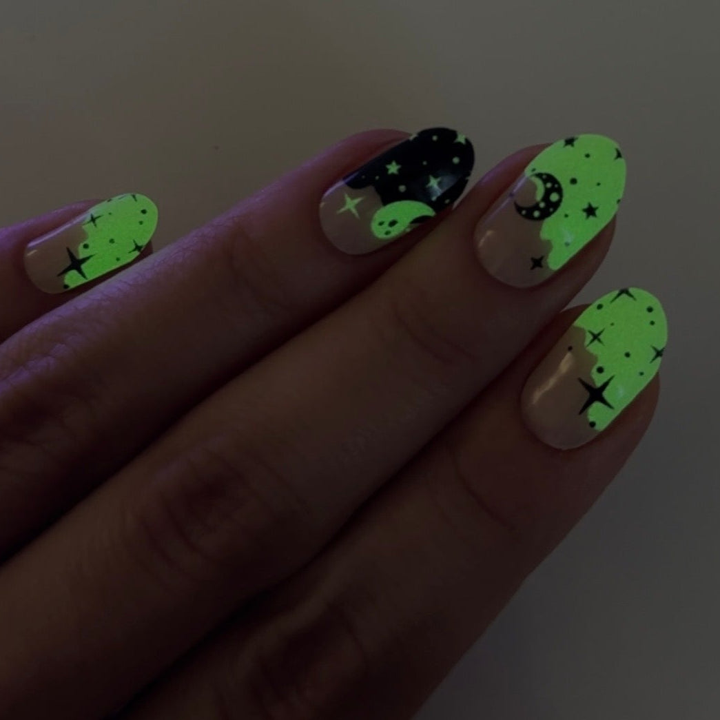 Hand with neon green glow in the dark
and black nail art on a plain background