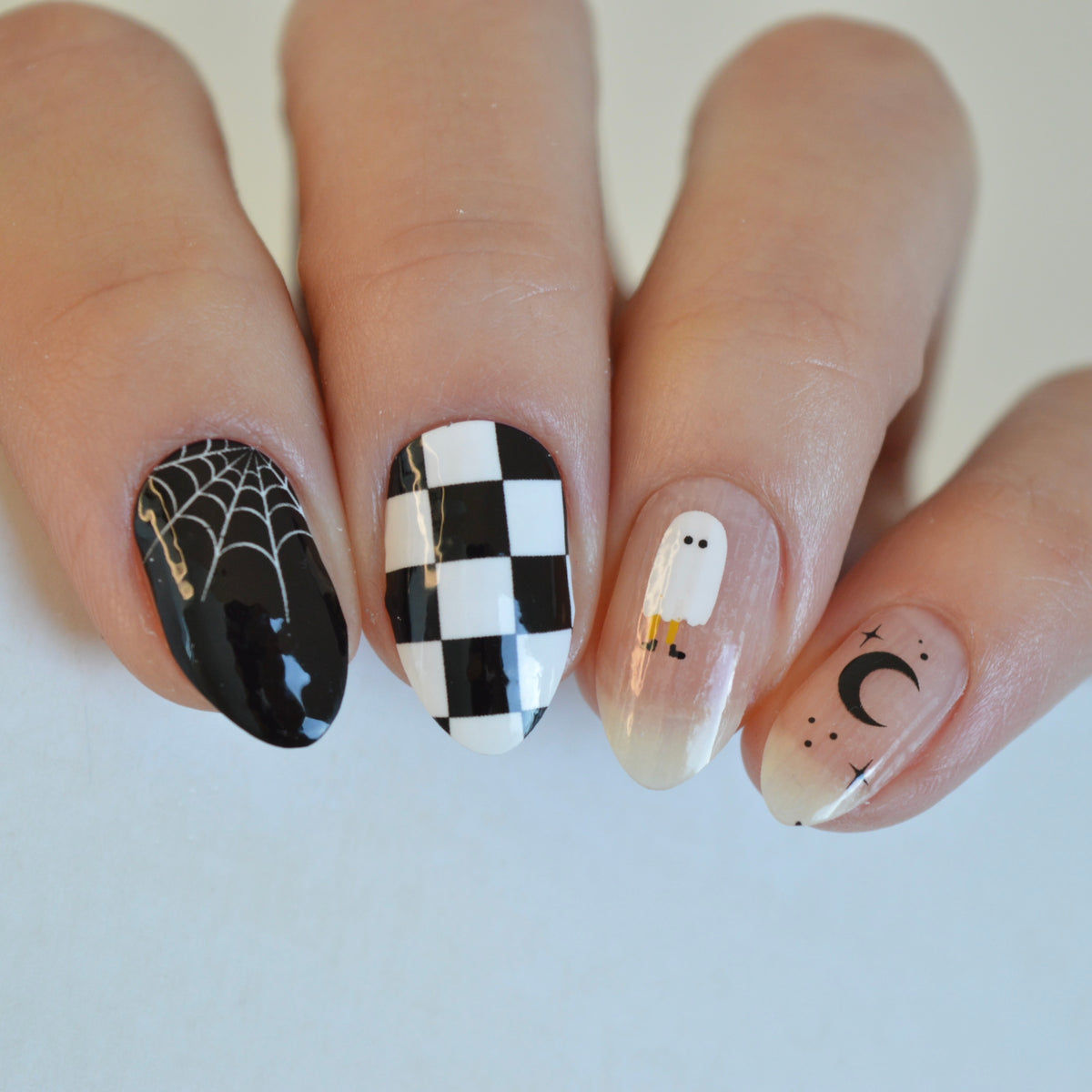 Casper nail wraps worn: spider web, checkerboard, ghost and moon nails