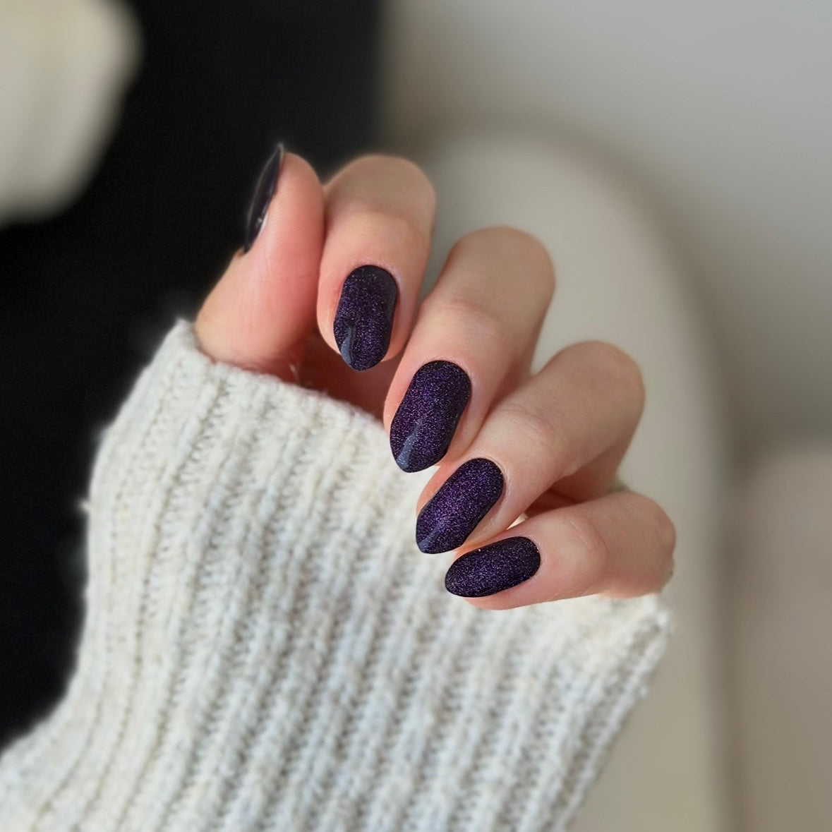 Hand in a knit sweater wearing Cat Eye Purple Super Jellies, deep purple cat-eye shimmer gel nails