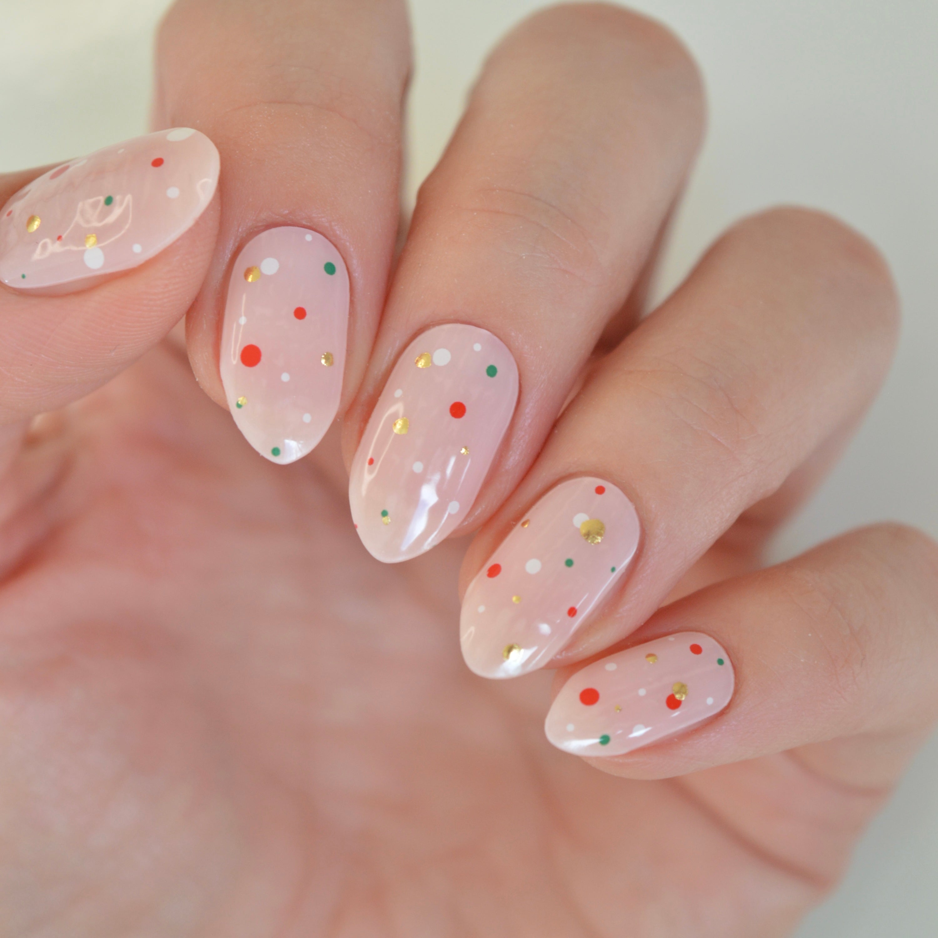 Hand wearing Freckles Super Jellies, sheer pink gel nails with red, green, white and gold dots