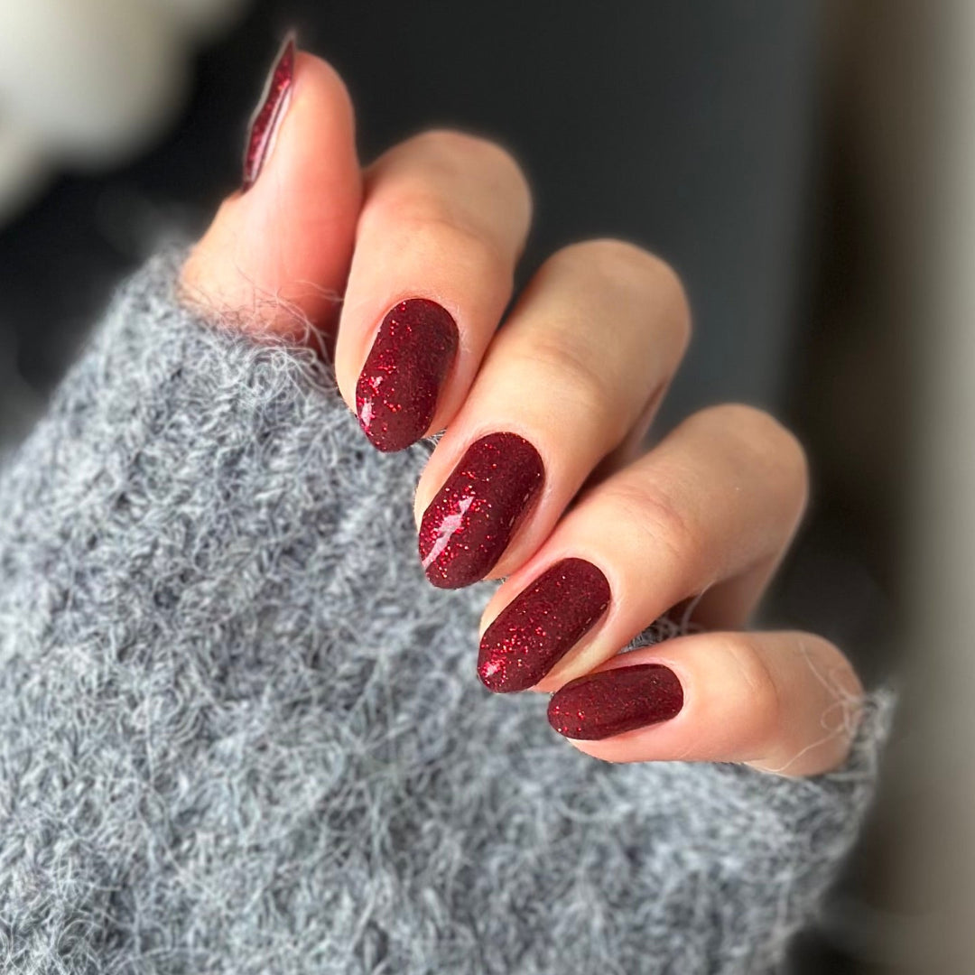 Hand with maroon glitter red christmas 
nail polish wearing a gray textured sleeve.